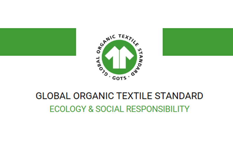 The official GOTS (Global Organic Textile Standard) logo, featuring a white T-shirt icon on a green circular background. Below the logo is the text "GLOBAL ORGANIC TEXTILE STANDARD" and "ECOLOGY & SOCIAL RESPONSIBILITY".